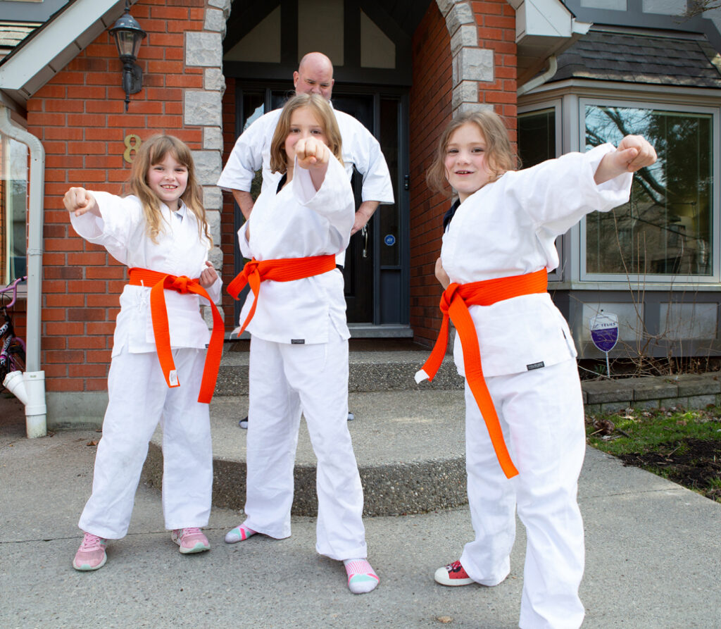 Trevor Parry standing proudly behind his three daughters posing in their karate uniforms.